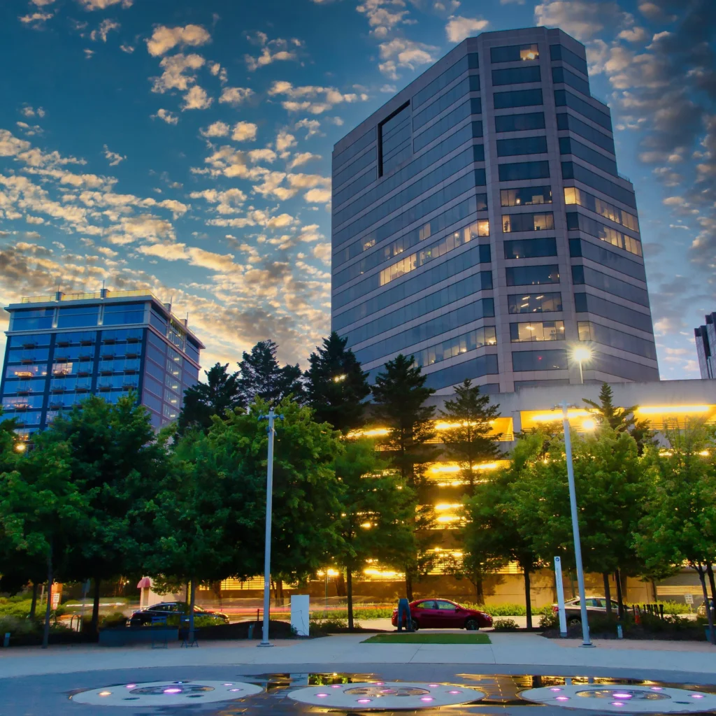 City buildings and a tree-lined street in Greensboro at dusk.