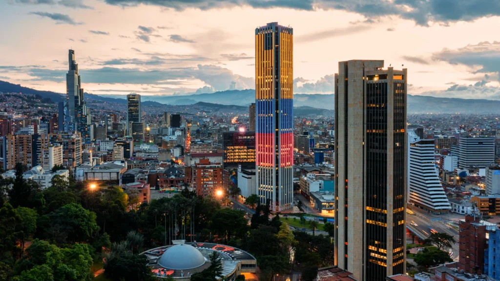 Bogotá skyline with high-rise buildings and mountains at dusk.