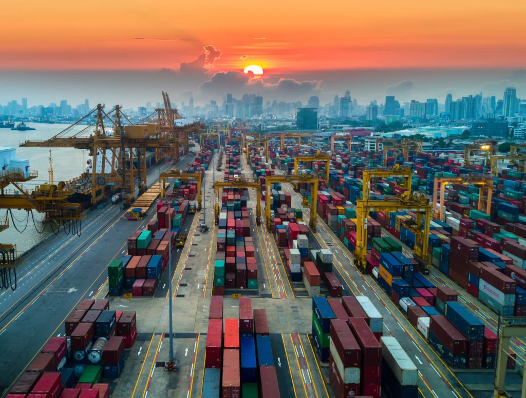 Shipping containers and cargo cranes at a port at sunset.