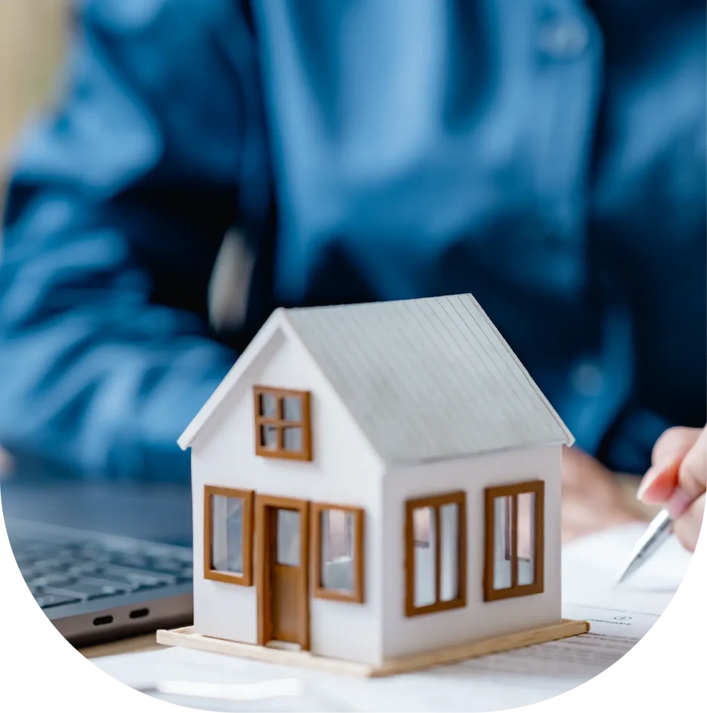 Person working beside a laptop and a miniature house.