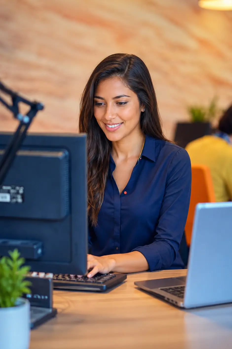 Woman working at a desk with a desktop monitor and laptop.