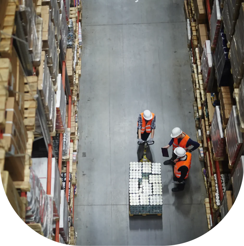 Overhead view of warehouse workers beside a pallet in a storage aisle.