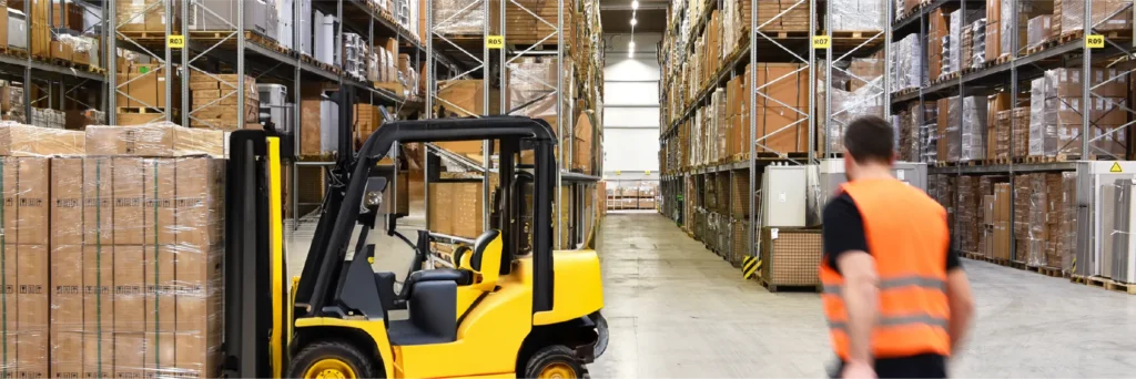 Forklift and worker in a high-visibility vest between warehouse shelves.