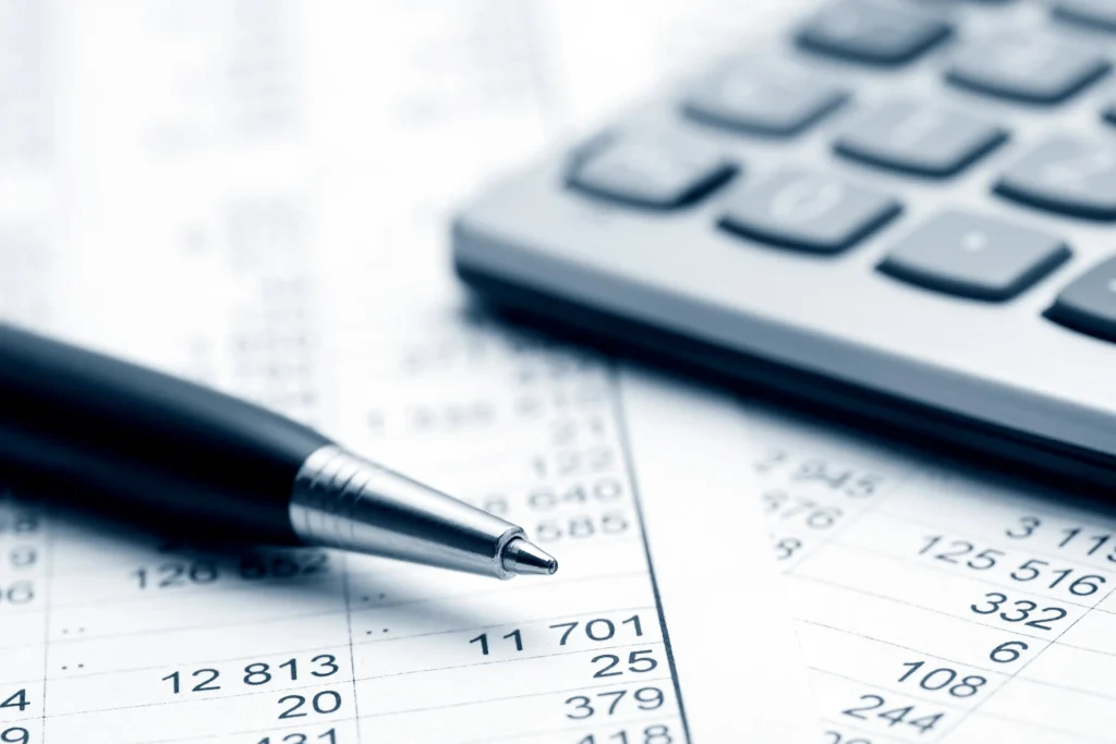 Pen, calculator, and rows of figures on financial paperwork.