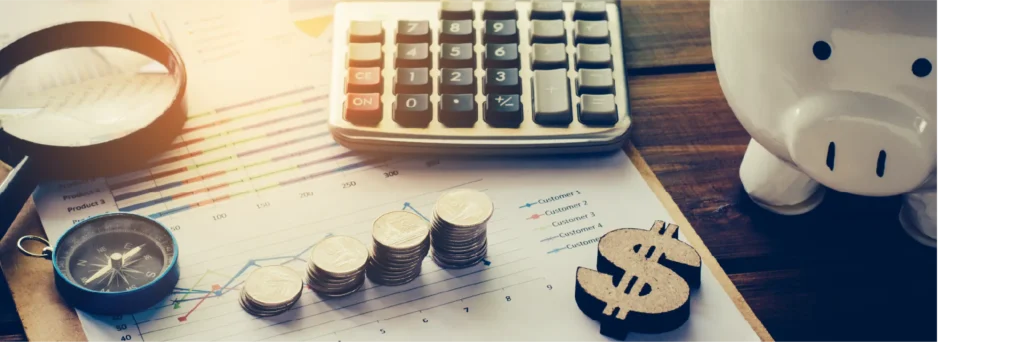 Calculator, coins, a magnifying glass, and a piggy bank on financial paperwork.